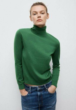 Maglione a collo alto verde in morbido tessuto a maglia, con maniche lunghe e una vestibilità aderente, abbinato a jeans di denim blu.