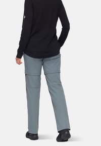 Graue, leichte Hosen mit Reißverschlüssen, die zu Shorts umwandelbar sind, kombiniert mit einem schwarzen Langarmoberteil und schwarzen Schuhen.