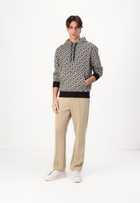 Black and white patterned hoodie with drawstring and pocket, paired with beige trousers and white sneakers. Smooth fabric, relaxed fit.