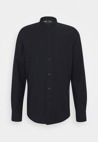 Zwarte longsleeve shirt met een bandkraag, knoopsluiting, één borstzak en een subtiele geborduurde detail aan de onderzijde links.