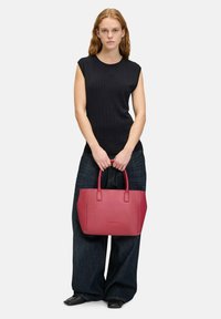 Czerwona skórzana torba na ramię o sztywnym kształcie i podwójnych uchwytach, zestawiona z czarnym, prążkowanym topem bez rękawów oraz luźnymi ciemnymi dżinsami.