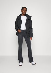 Black puffer jacket with a high collar, white t-shirt, dark grey flared jeans, and white sneakers with black and orange accents.