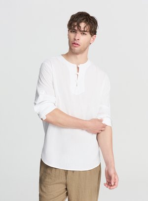 Camicia bianca con bottoni in tessuto leggero, con orlo arrotondato, tre bottoni all'altezza del collo e maniche arrotolate.