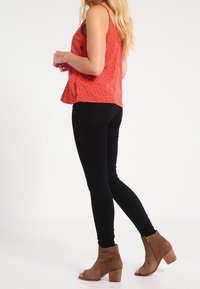 Röd ärmlös topp med små svarta mönster, kombinerad med svarta skinny jeans och beige ankelskängor med klack. Slät struktur hela vägen.