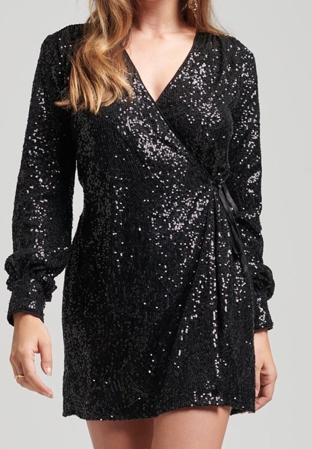 Femme portant une robe portefeuille noire à sequins avec des manches longues resserrées aux poignets et un profond décolleté en V.