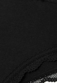 Un material textil negru cu o textură netedă are o dantelă cu margini ondulate pe toată lungimea, oferind un detaliu contrastant.