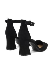 Scarpe con tacco alto in suede nero, con punta rotonda, cinturino alla caviglia e tacco spesso. Superficie liscia con una leggera texture e dettagli minimi.