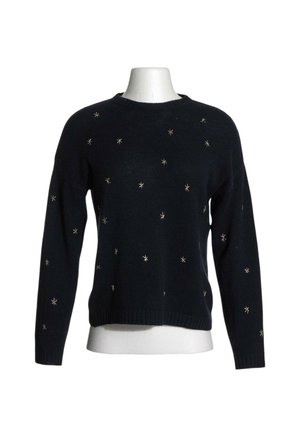 Jersey negro de manga larga con pequeños adornos plateados en forma de estrella dispersos por el frente y las mangas sobre un torso de maniquí blanco.