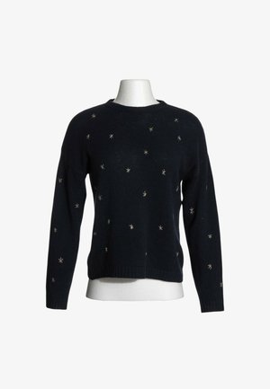 Jersey negro de manga larga con pequeños adornos plateados en forma de estrella dispersos por el frente y las mangas sobre un torso de maniquí blanco.