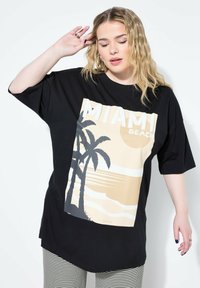 Mustapohja-yläosa, jossa on Miami Beach -grafiikka vaaleanruskeana ja mustana, kuvastaa palmupuita ja auringonlaskua. Valmistettu pehmeästä puuvillamateriaalista.
