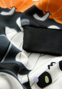 Felpa caratterizzata da una stampa grafica colorata con un design di cartone animato in arancione, nero e bianco, con un polsino a costine nere texturizzate.