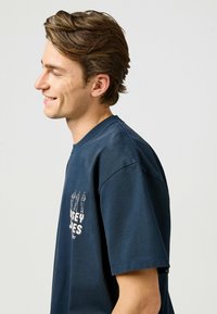 Camiseta de algodón azul marino con cuello redondo y mangas cortas, con estampado gráfico blanco en el frente. Textura suave y corte relajado.
