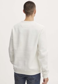 Witte sweatshirt met een ronde hals, ribgebreide mouwen en onderkant. Stof heeft een zachte textuur. Zichtbare naden en een klein detail op de rug.
