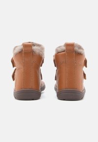 Bottines en cuir marron avec doublure en fourrure douce, sangles réglables et semelle en caoutchouc grise. Texture lisse avec accents cousus.