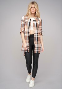 Langærmet skjorte i tern med nuancer af brun, sort og hvid, parret med sorte leggings og hvide sneakers; ternet mønster med knaplukning.