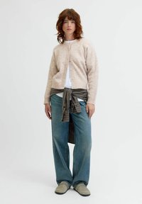 Ljusrosa ullkofta med knappar, kombinerad med en vit skjorta. Blå vida jeans och en svartvit rutad skjorta knuten i midjan.