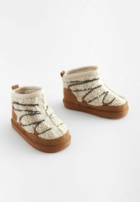 Stivaletti alla caviglia di pelliccia color crema con accenti in suede marrone, caratterizzati da una superficie testurizzata e fasce elastiche verde scuro per una vestibilità sicura.