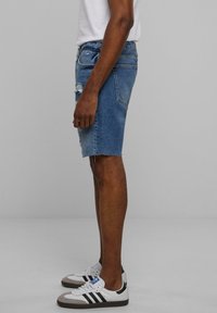 Siniset denim-shortsit, joissa on revitty helma ja kulutustyyliset yksityiskohdat. Yhdistetty valkoisiin ja harmaisiin tennareihin, joissa on mustia yksityiskohtia.