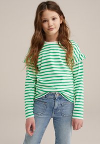 Grön och vit randig långärmad skjorta med volangärmar, kombinerad med blå jeans med en klassisk femfickdesign.
