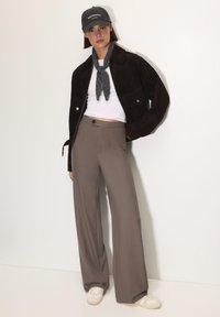 Barna velúr dzseki, fehér ing, szürke sál és bő szabású barna nadrág. Fehér sneakers bézs részletekkel. Sapka "MONTMARTRE PARIS" felirattal.