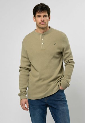 Camiseta de manga larga de punto waffles en verde oliva claro con tapeta de tres botones y pequeño logo. Presenta un corte relajado y una textura suave.