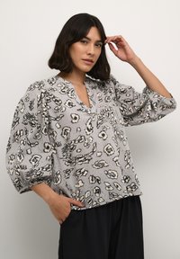 Blusa grigia con maniche a sbuffo, caratterizzata da un motivo astratto in nero e crema, scollo a V, tessuto testurizzato e vestibilità comoda.