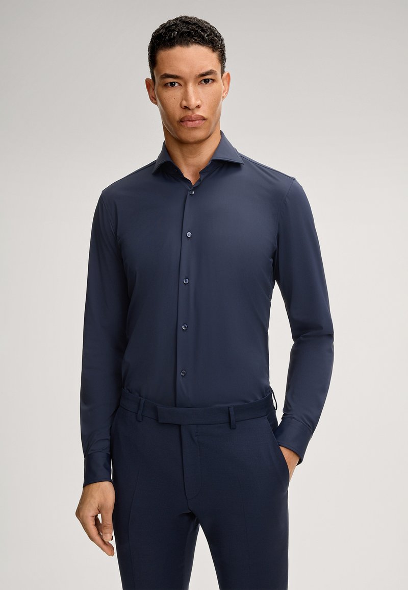 Marineblauw longsleeve shirt van een gladde stof, met een verspreide kraag, knopen aan de voorkant en een slim fit, gecombineerd met bijpassende donkere broek.