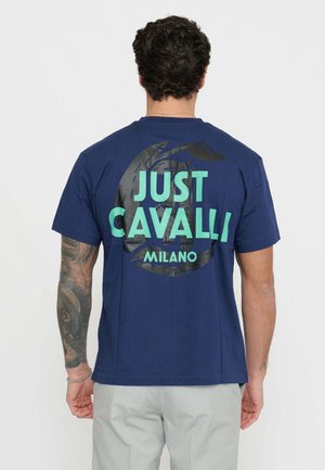 Granatowa bawełniana koszulka z dużym zielonym napisem "JUST CAVALLI" oraz "MILANO" z tyłu, z teksturowanym czarnym okrągłym wzorem graficznym.