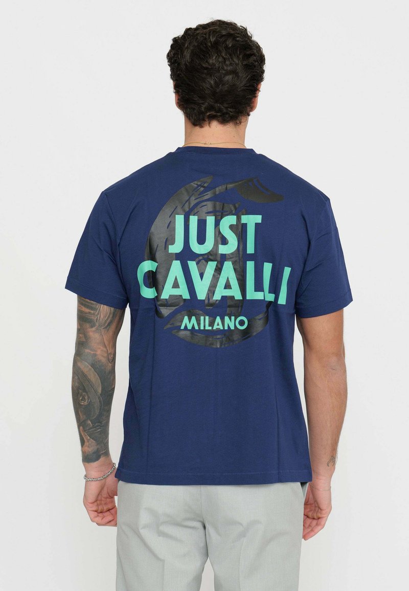 Granatowa bawełniana koszulka z dużym zielonym napisem "JUST CAVALLI" oraz "MILANO" z tyłu, z teksturowanym czarnym okrągłym wzorem graficznym.