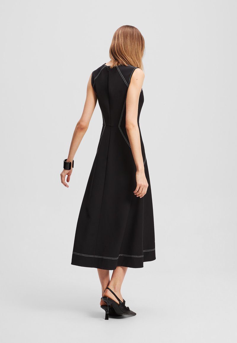 Schwarzes ärmelloses Kleid mit einem enganliegenden Oberteil und einem ausgestellten Midirock, der kontrastierende weiße Nähte und eine glatte Textur aufweist.