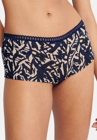 Bomulds-pige-shorts med et navyblåt og sort abstrakt bladmønster på en cremefarvet baggrund. Blondekant ved linningen. Blødt, elastisk materiale.