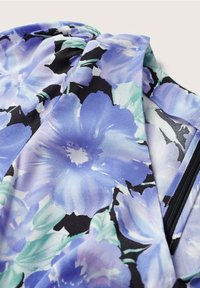 Textil s květinovým vzorem v odstínech levandulové a tyrkysové, obsahující velké květiny a zelené listy na černém pozadí, s hladkým povrchem.