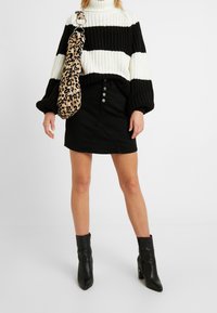 Czarny i biały sweter w paski z dzianiny, czarna spódnica dżinsowa z zapięciem na guziki, torba w zwierzęcy wzór i czarne botki za kostkę.