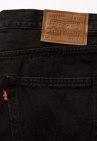 Jean Levi's en denim noir montrant la poche arrière, l'étiquette rouge Levi's et la pièce en cuir marron avec la taille W32 L32.