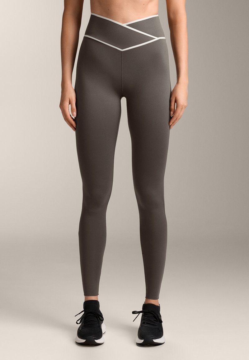 Szürke, magas derekú leggings, melynek derék részén fehér, keresztbe rakott részletek találhatóak. Rugalmas anyagból készült, sima tapintású és szoros fazonú.