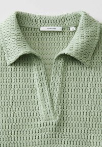 Haut en crochet vert clair avec col et encolure en V, montrant l'étiquette de marque "OPUS" et l'étiquette de taille 36 à l'intérieur du col.