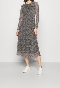 Robe longue à manches longues en fleurs avec un corsage ajusté et une jupe midi fluide ; fond noir avec de petites fleurs blanches et roses ; manches transparentes, associée à des baskets blanches.