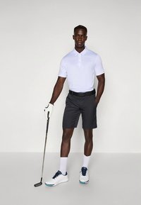 Polo branca de manga curta, calções escuros, sapatos de golfe brancos com detalhes azuis, segurando um taco de golfe, usando uma luva. Design simples e desportivo.