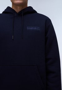 Felpa con cappuccio blu navy realizzata in tessuto morbido, con tasca frontale, cappuccio regolabile con cordino e logo ricamato "NAPAPIJRI geographic" sul petto.