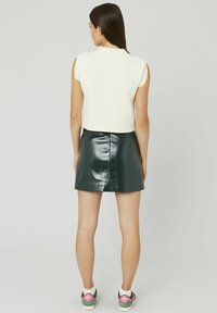 Crop top blanc texturé associé à une mini-jupe en cuir verni verte. Le modèle porte des baskets vertes et roses. Design simple, sans motifs visibles.