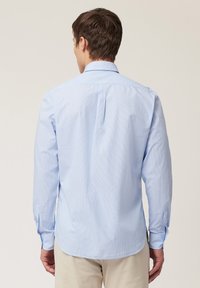 Lichtblauwe, lange mouwen blouse met een knoopsluiting en subtiele verticale strepen. Heeft afgeronde zomen en manchetten.