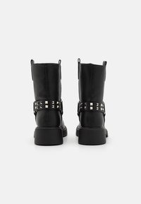 Bottes noires en cuir montantes avec un talon épais, des détails de sangle cloutée et des tirettes pour un enfilage facile.