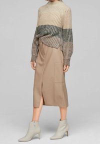 Maglione lavorato a maglia con colori sfumati beige e oliva, abbinato a una gonna midi beige con spacco laterale e tasca applicata, e stivaletti grigi alla caviglia.