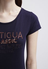 Námořnická modrá bavlněná tričko s krátkým rukávem a kulatým výstřihem, který má flitrové nápisy v odstínech růžového zlata a metalické akcenty.