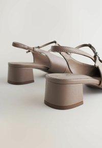 Sandales à talons beiges avec un talon carré bloc, des lanières fines et un design minimaliste. Texture en cuir lisse avec une finition polie.