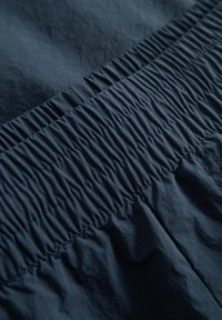 Tessuto blu navy con dettagli in elastico arricciato. Superficie liscia e leggermente testurizzata, che mostra cuciture uniformi e una leggera lucentezza.