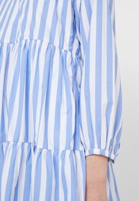 Blau-weißer gestreifter Kleid mit puffärmel, geraffter Taille und mehrlagigem Design. Hergestellt aus leichtem Stoff mit einer glatten Textur.