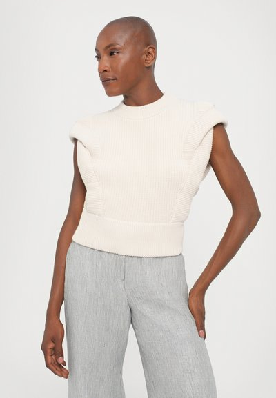 Knit sleeveless top in light beige, featuring rounded shoulders and ribbed texture. Paired with pinstriped, wide-leg trousers in soft fabric.