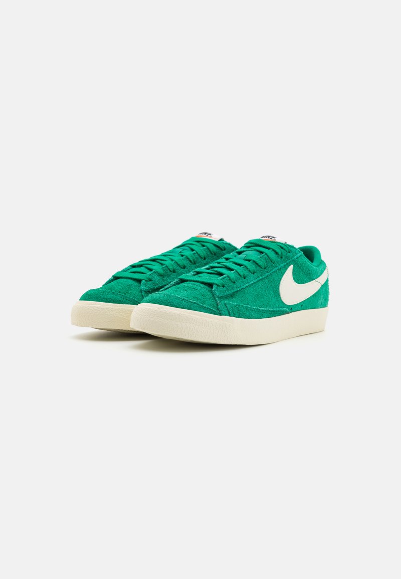 Zapatillas deportivas de ante verde con parte superior texturizada, el logo de Nike en blanco, cordones planos y suela de goma crema, presentando un diseño de corte bajo.