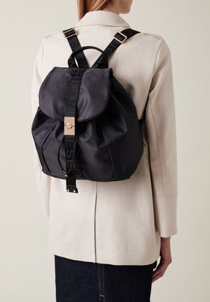 Schwarzer Rucksack aus strukturiertem Stoff, mit einer runden Klappe, goldfarbenen Beschlägen und verstellbaren Trägern mit einem Logomuster.